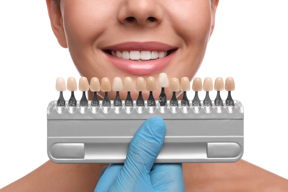 Doctor checking young woman's teeth color on white background, closeup. Cosmetic dentistry