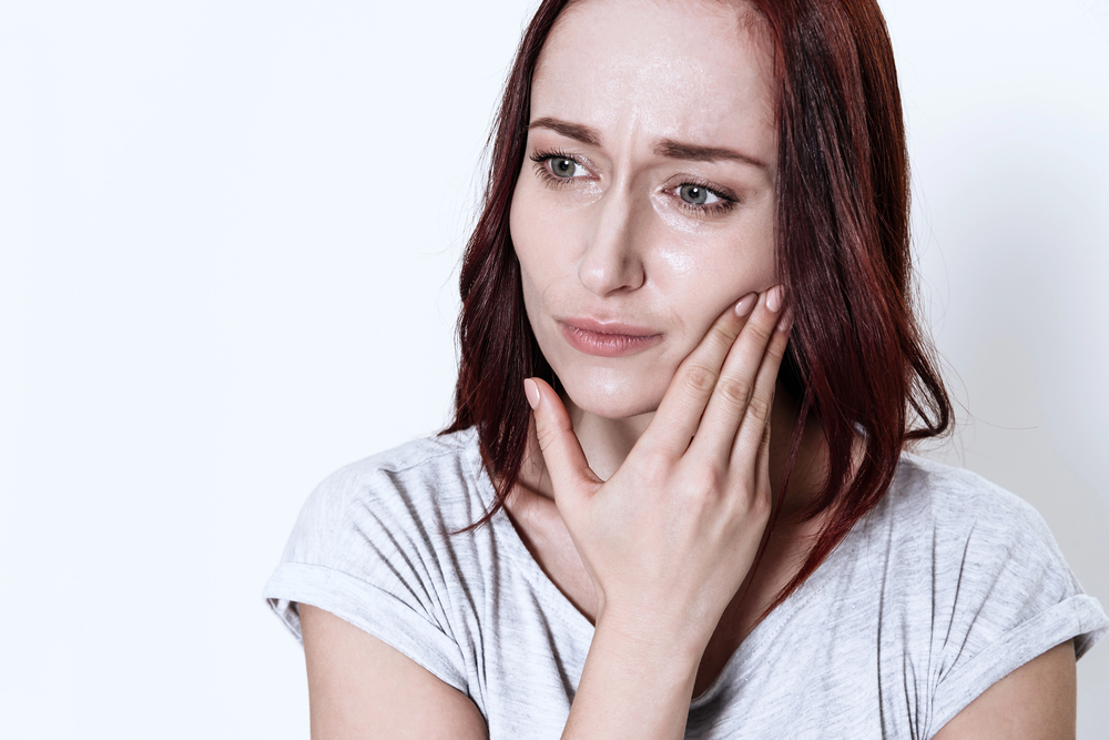 woman with brown hair touching her jaw because of pain
