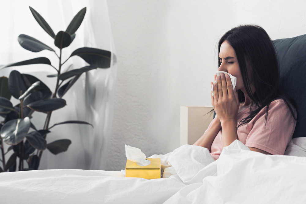Sick young woman with box of paper napkins sitting in bed