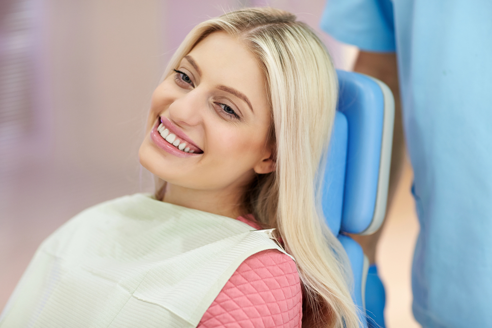 young woman with blonde hair sitting in dentists chair for checkup smiling