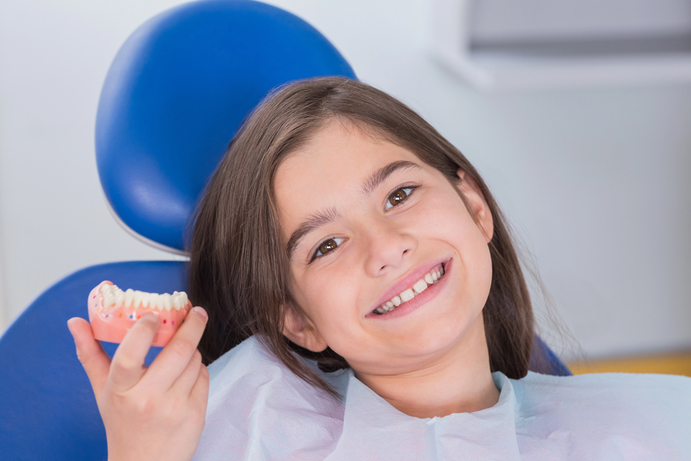young girl in dentist chair holding model of lower jaw