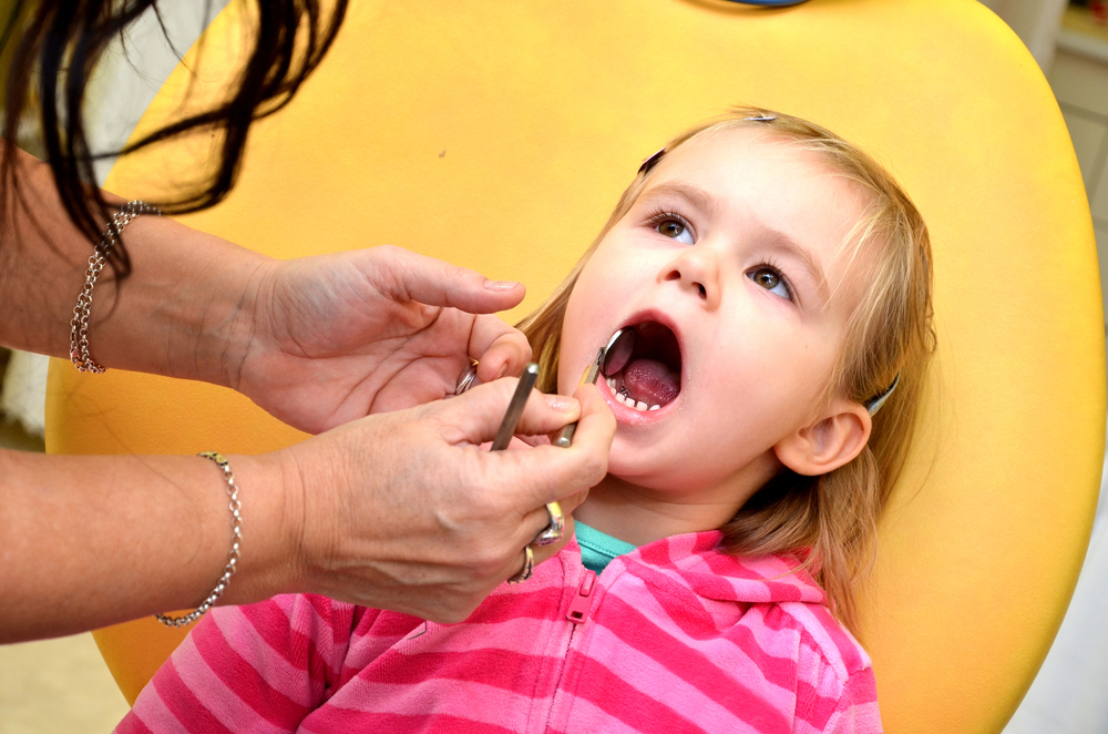 toddler child's first dentist appointment in yellow dental chair and pink shirt
