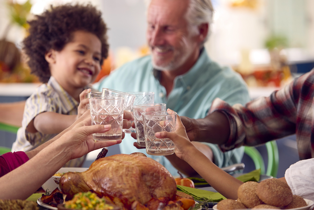 multigenerational family celebrating Thanksgiving at home eating a meal and doing a cheers with water