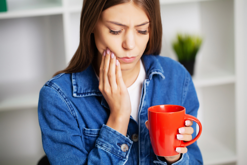 woman experiencing dental pain, holding a red coffee cup